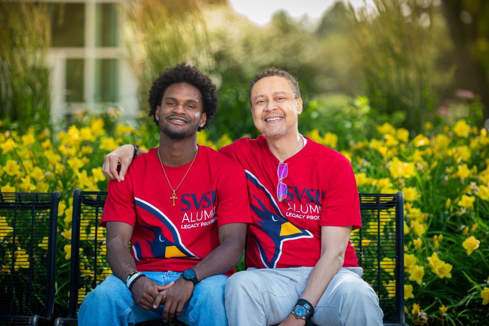 Father and son sitting on a bench at SVSU with flowers behind them
